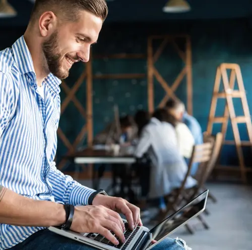 Mann som smiler mens han jobber på laptop, og nyter en produktiv og positiv arbeidsdag